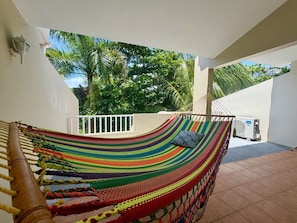 A hammock on a balcony with a view of palm trees and a white railing.