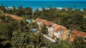Zona residencial costera con casas de techo de teja terracota, una piscina y densa vegetación tropical.