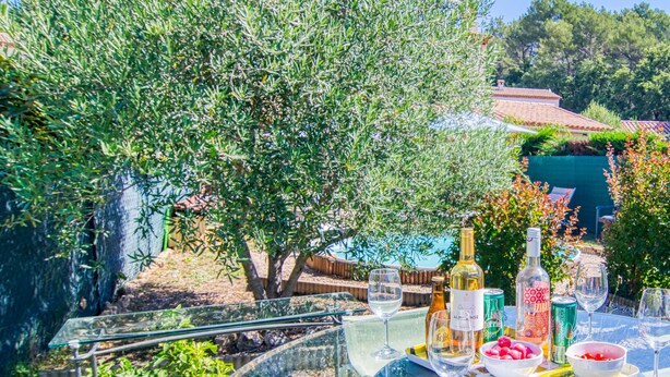 An outdoor dining area with a table set for a meal, surrounded by olive trees and a view of a house. - Villa Les Genêts by Interhome (Montauroux)