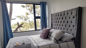 A neatly made bed with a grey headboard, a checkered bedspread, and a rolled white towel with toiletries.
