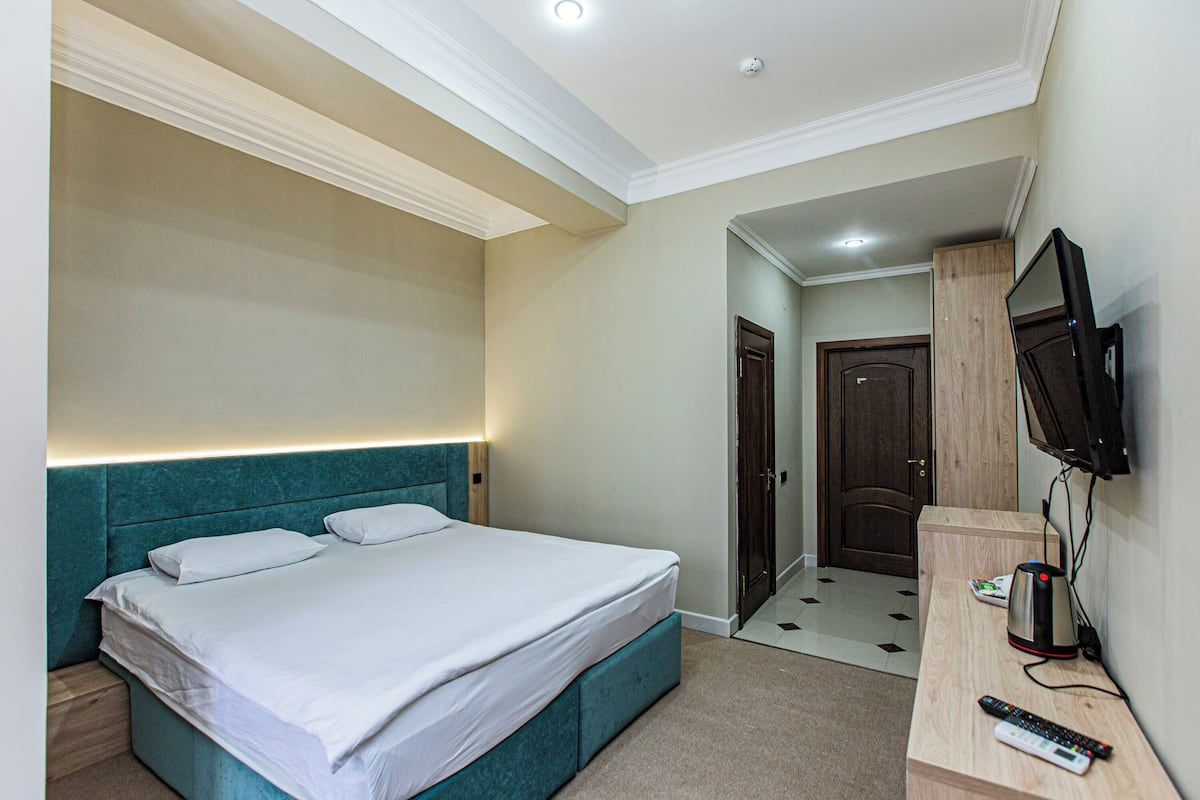 A hotel room with a bed, a TV mounted on the wall, and a desk with a remote control.