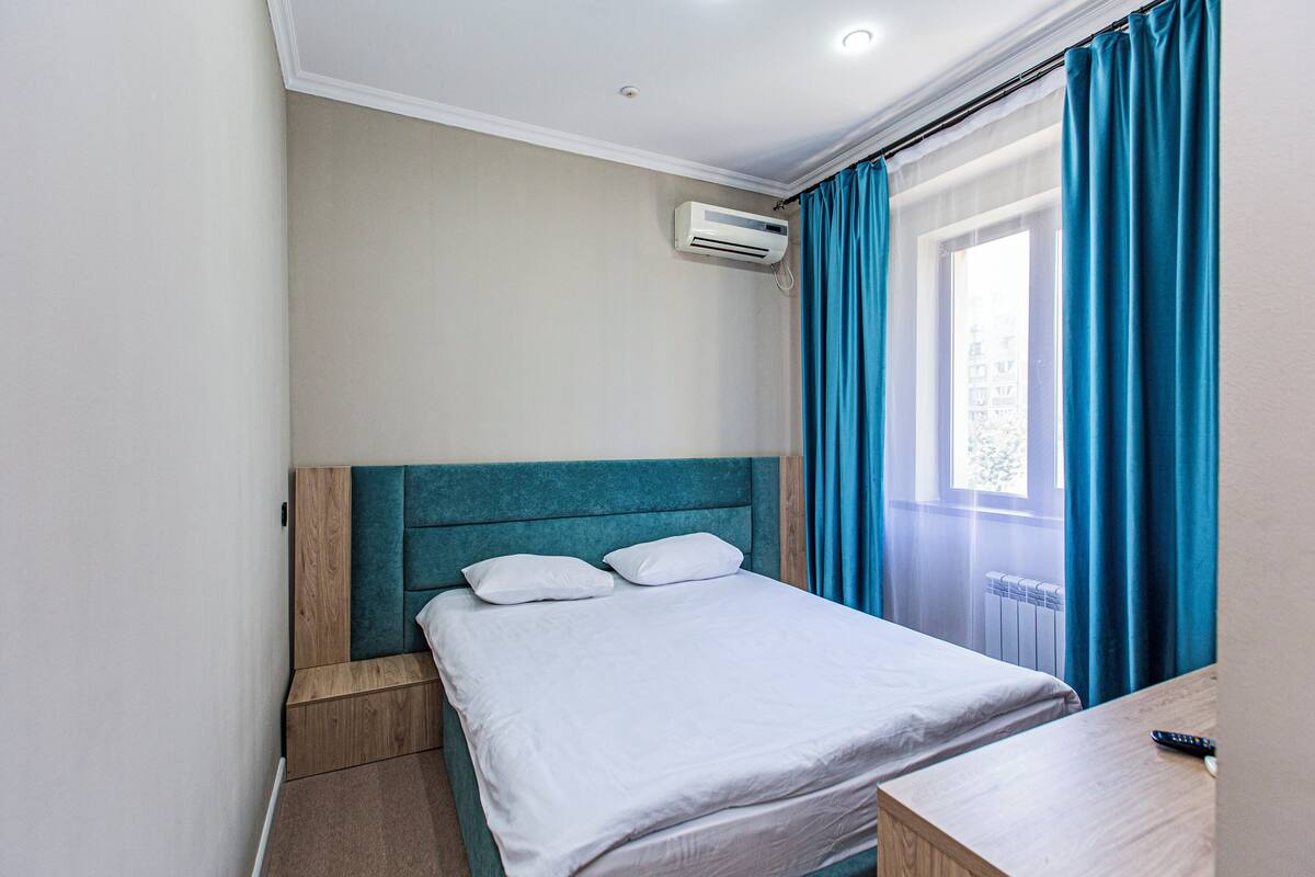 A neatly made bed with white bedding, a wooden headboard, and a small wooden nightstand with a remote control.