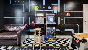 A room with a black and white checkered floor, a brown leather couch, a small wooden stool, and arcade games themed around space and Pac-Man. - Totally 80"s Hideaway (Savannah)