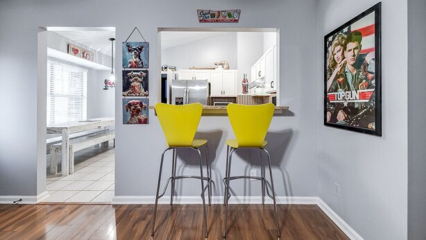 A modern kitchen with white cabinets, a stainless steel refrigerator, and a yellow bar stool. - Totally 80"s Hideaway (Savannah)