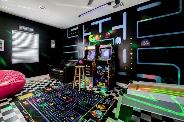 A retro-themed room with arcade games, a neon sign, and a checkered floor.