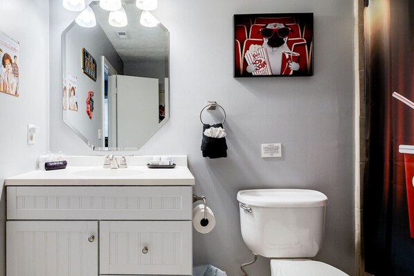 A bathroom with a white sink, mirror, toilet, and a framed picture of a dog wearing sunglasses. - Totally 80`s Hideaway (Savannah)
