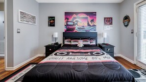 A bedroom with a bed, two bedside tables, a ceiling fan, and a wall with various posters and a clock. - Totally 80"s Hideaway (Savannah)