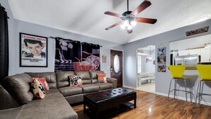 A living room with a sofa, coffee table, and a ceiling fan. There is a kitchen area with a dining table and chairs. - Totally 80"s Hideaway (Savannah)