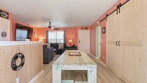 Een gezellige woonkamer met een houten tafel, banken en een plafondventilator.
