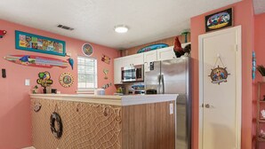 Een keuken met een houten kookeiland, witte kasten, een koelkast en diverse wanddecoraties.
