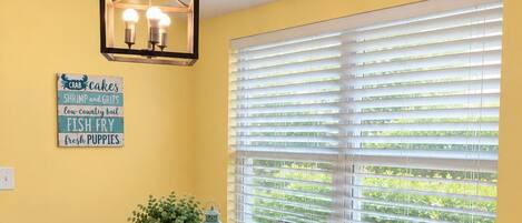 A dining area with a wooden bench and table, a hanging light fixture, and a window with blinds.