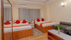 A hotel room with two wooden beds, a gray sofa, a small table, and a mirror. - Hotel Tiktok (Kathmandu)