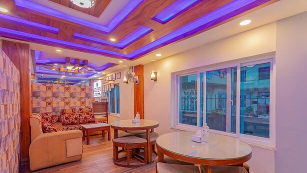 A cozy living area with a sofa, a round table, and chairs, wooden flooring, and a large window with a view. - Hotel Tiktok (Kathmandu)