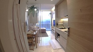 A modern kitchen with a built-in oven, a sink, and a countertop. There is a dining area with a table and chairs, and a large window providing a view of the outdoors. - Rocco 513 - Corner 1 Bedroom Serviced Apartment With Seaview (Krabi)