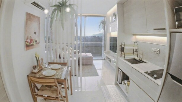 A modern kitchen with white cabinetry, a dining area with a table and chairs, and a large window offering a view of the outdoors. - Rocco 513 - Corner 1 Bedroom Serviced Apartment With Seaview (Krabi)