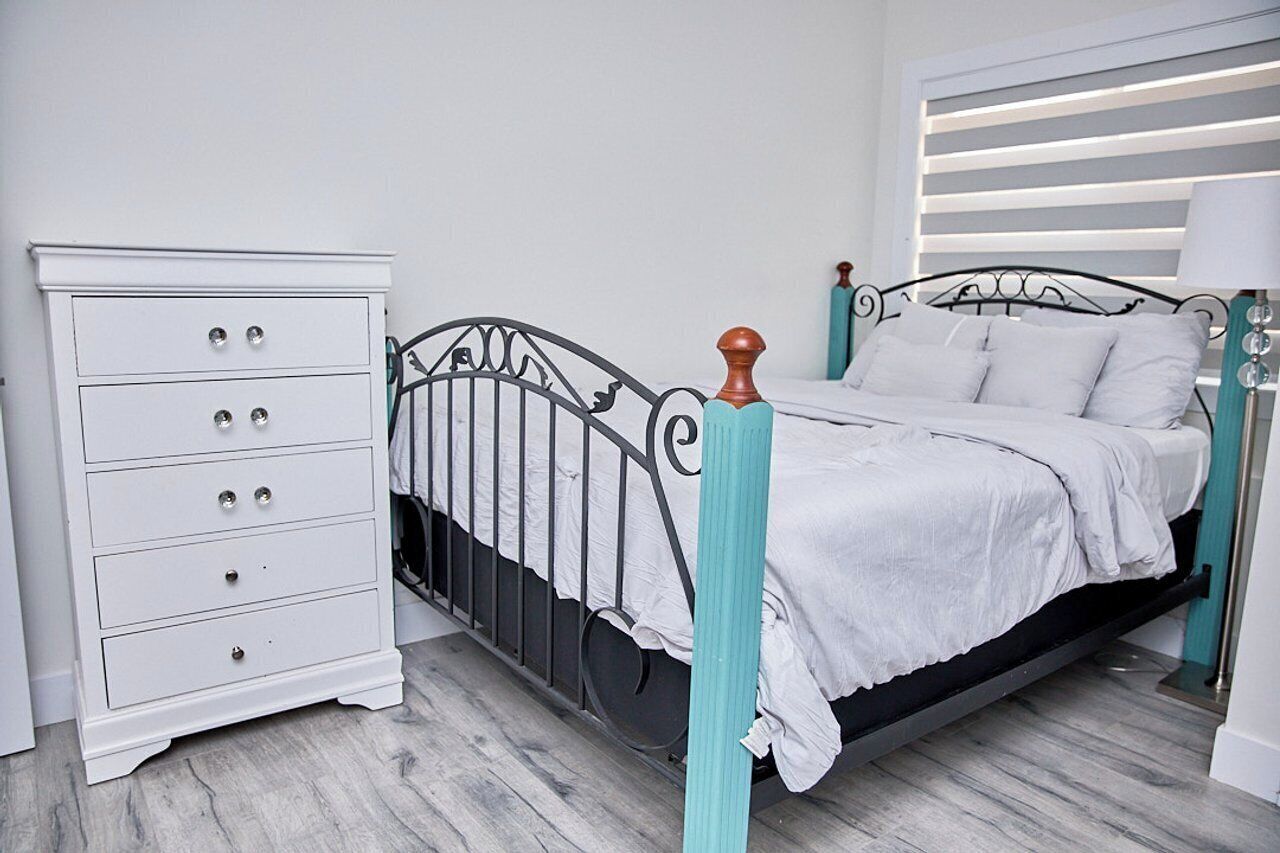 A bedroom with a bed, a white dresser, and a nightstand.