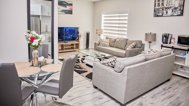 A modern living room with a glass coffee table, grey sofa, and a flat-screen TV. - Cozy 3-bedroom, 3 queen beds ground level suite in a desirable location in PG.  (Prince George)