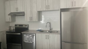 A modern kitchen with white cabinetry, stainless steel appliances, and a tiled backsplash. - Cozy 3-bedroom, 3 queen beds ground level suite in a desirable location in PG.  (Prince George)