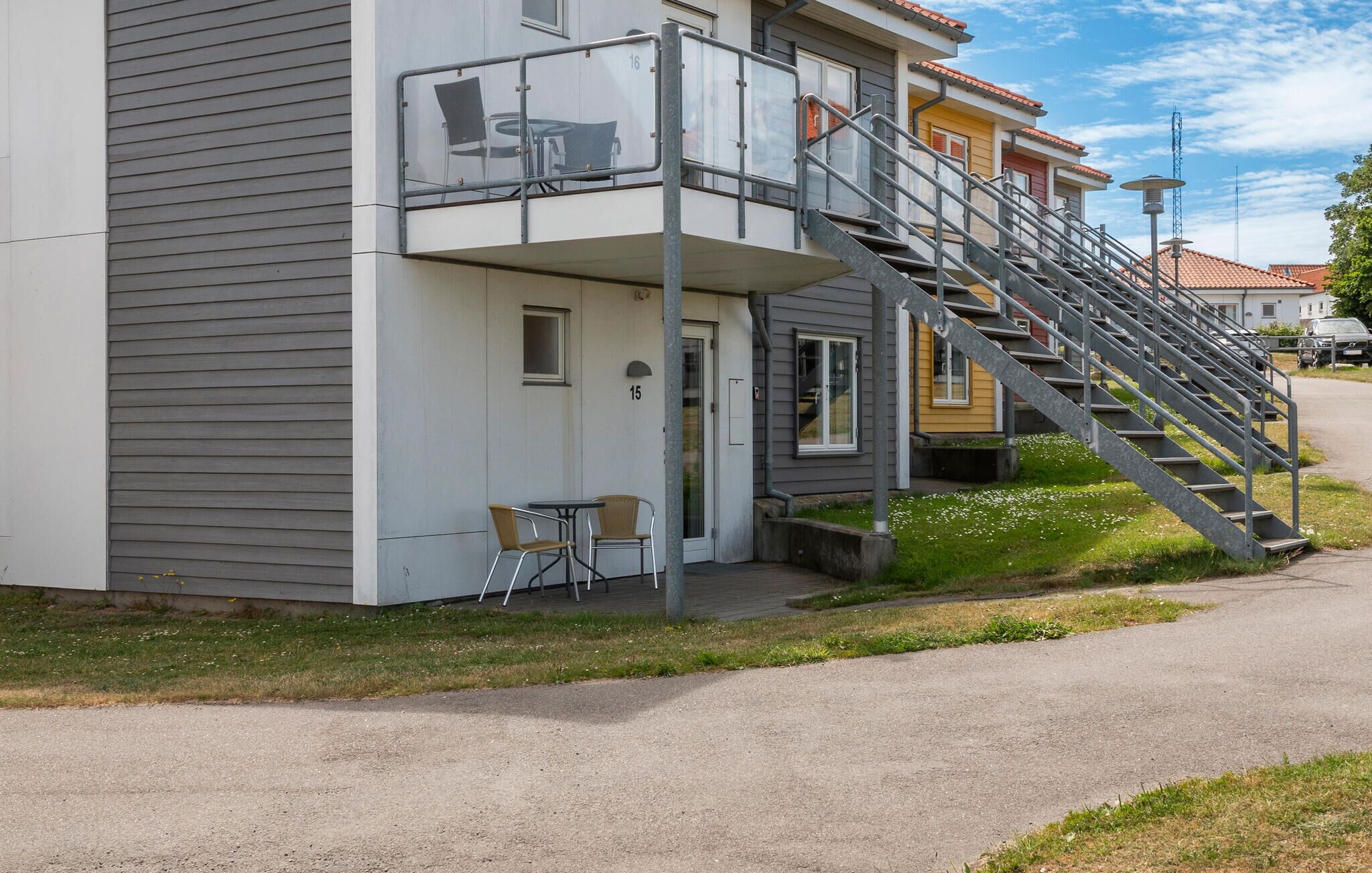 A residential building with a grey exterior, a balcony with a chair, and a staircase leading to the entrance.