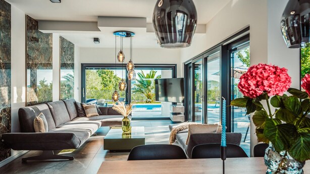 Un soggiorno moderno con divano, tavolino e vista su una piscina e vegetazione.