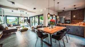 Una cucina moderna con isola in legno, una zona pranzo con tavolo e sedie in legno, e un soggiorno con divano e tavolino.