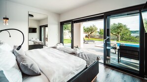 A modern bedroom with a large bed, a bedside table, a mirror, and a view of an outdoor pool area. - Lovely home in Razanac (Razanac)