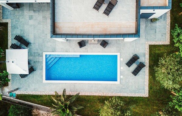 An aerial view of a modern outdoor swimming pool area with lounge chairs and a covered seating area. - Lovely home in Razanac (Razanac)