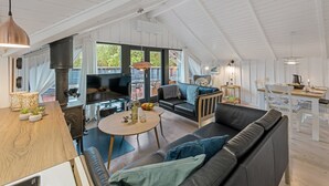 Un loft espacioso con techo alto, una zona de estar acogedora con sofá y sillones, una mesa de comedor y una cocina con un ventanal grande.