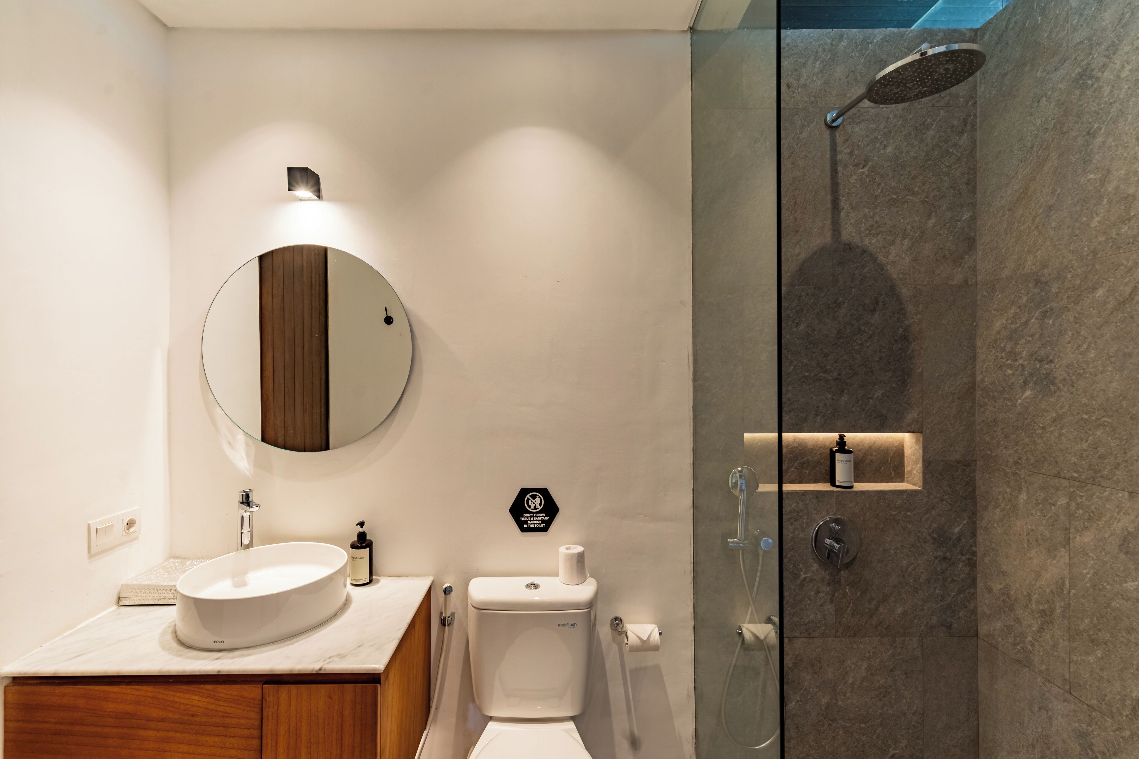 Un bagno moderno con uno specchio rotondo, un lavandino, un water e una cabina doccia in vetro.