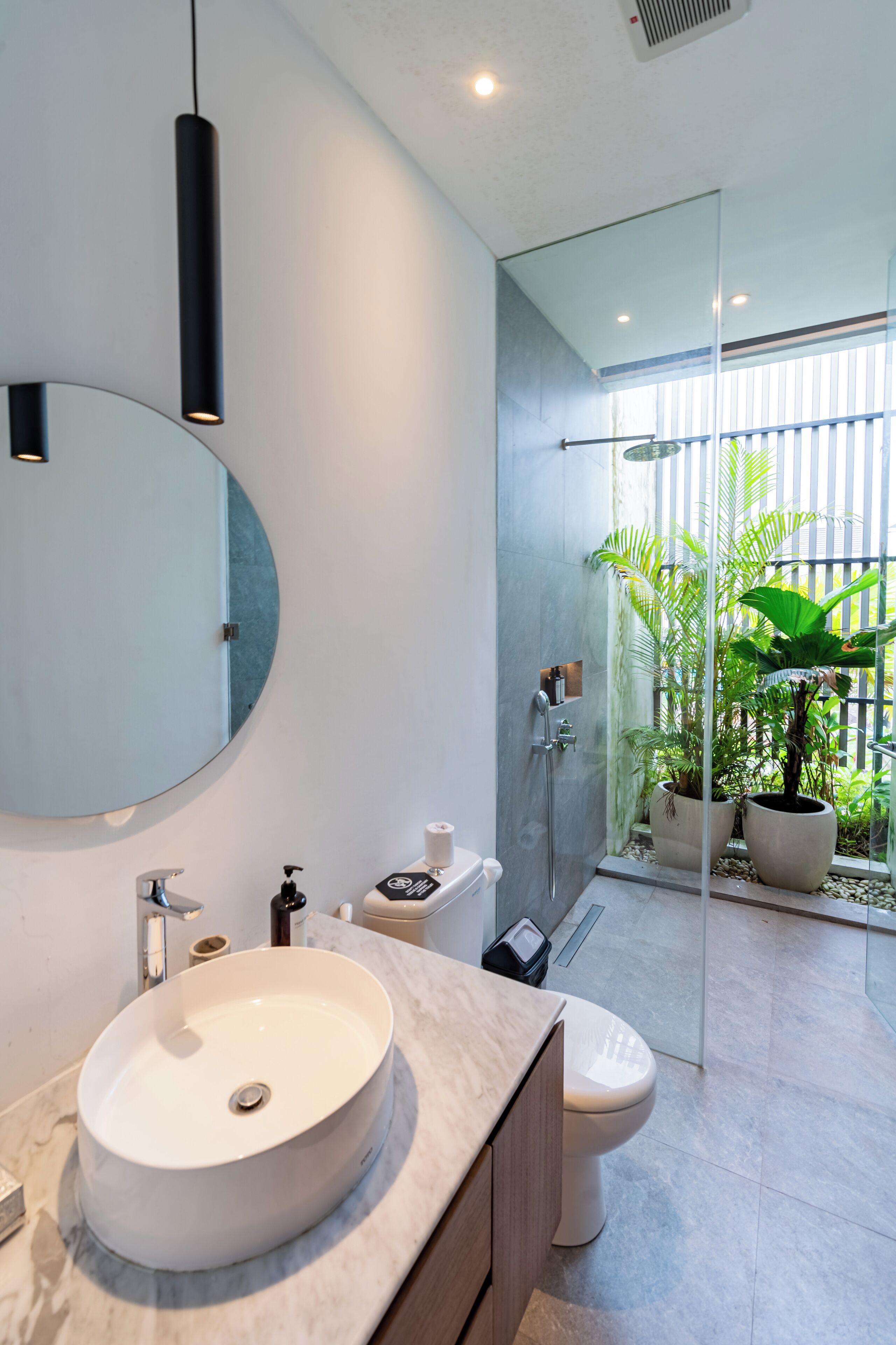 A modern bathroom with a round sink, a toilet, and a glass shower enclosure.
