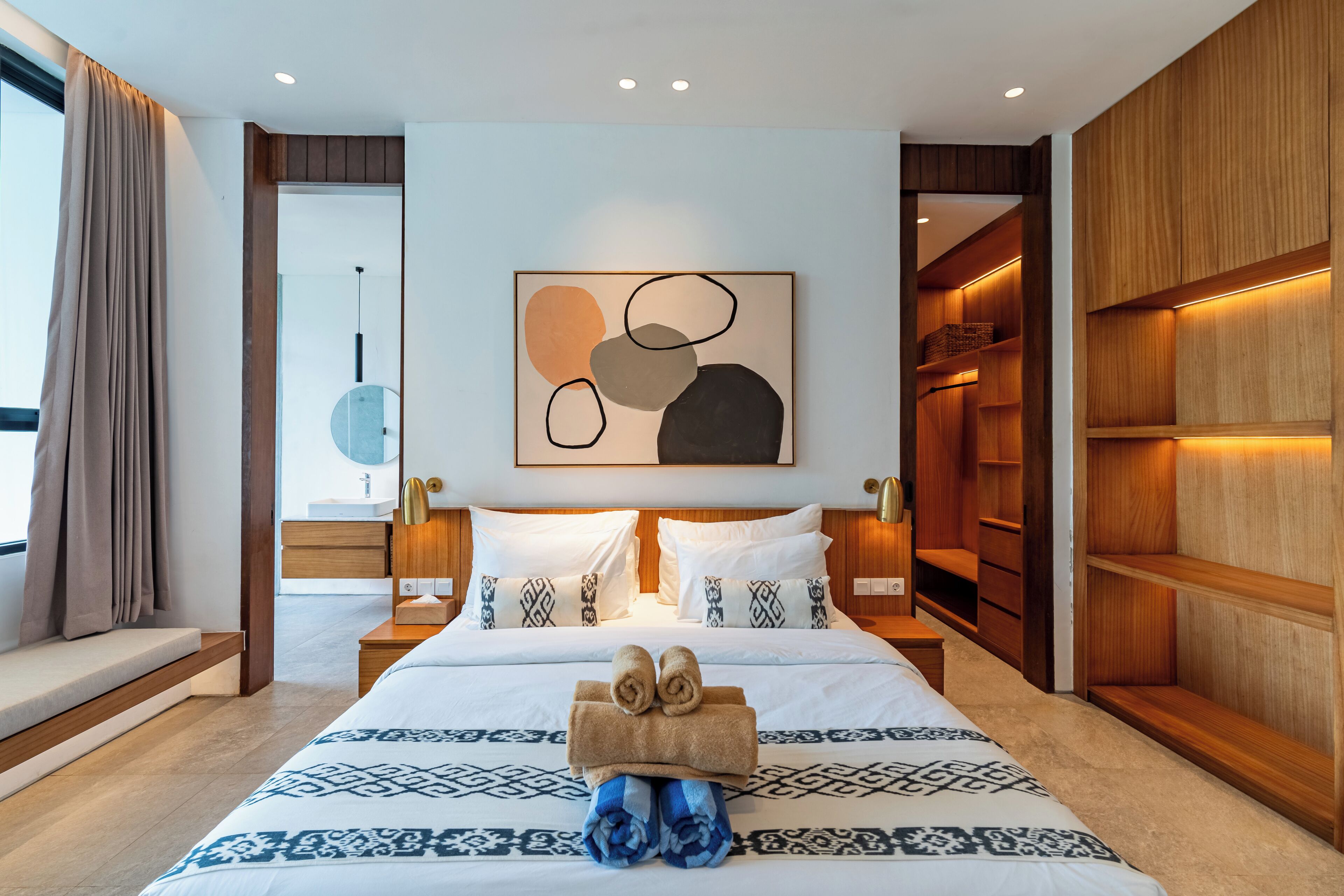 A modern hotel room with a large bed, wooden wardrobe, and a bedside table with a lamp.