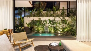 Zona relax esterna moderna con piscina, circondata da vegetazione rigogliosa e una cascata.