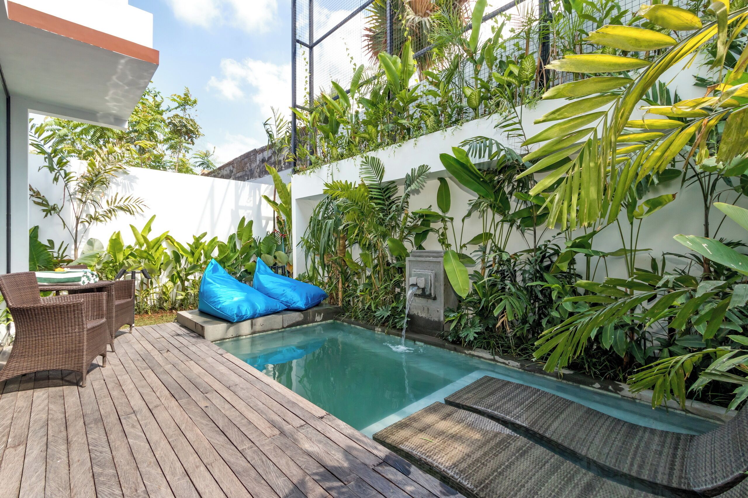 A pool area with a wooden deck, wicker furniture, and a blue bean bag.