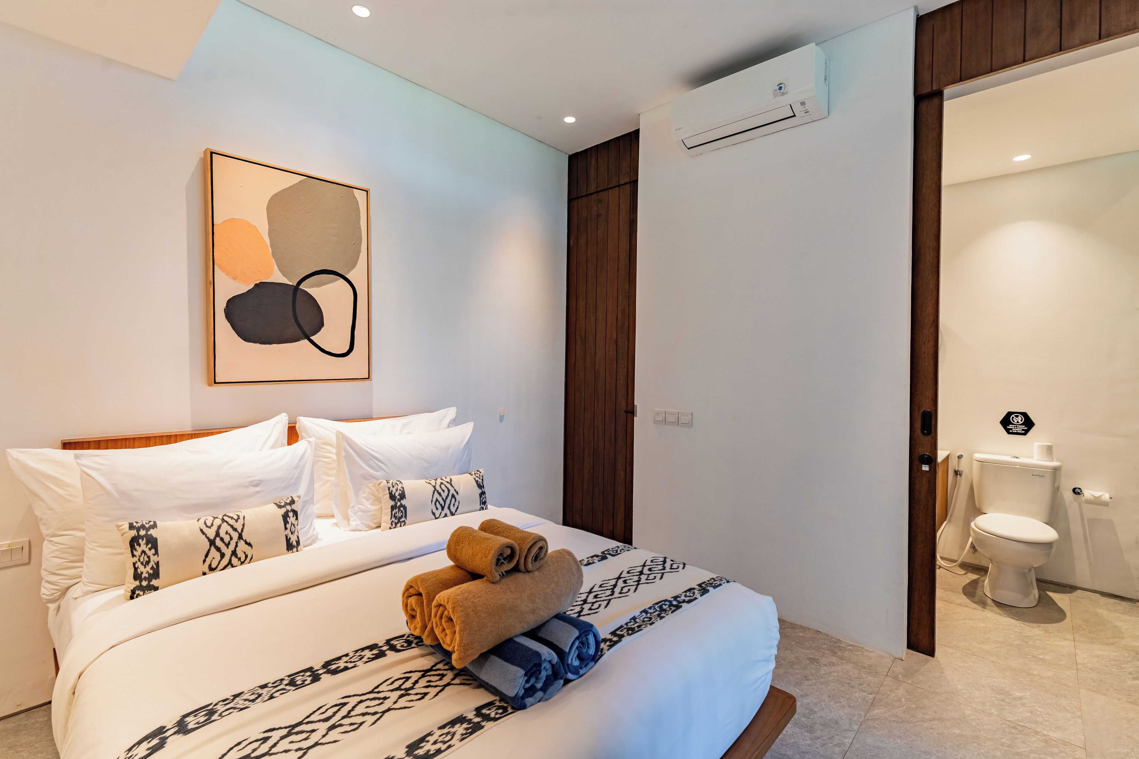 Een moderne hotelkamer met een net opgemaakt bed, een groot abstract schilderij en een zichtbare badkamer met toilet en douche.