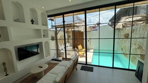 A modern room with a large window, a sofa, a TV, and a pool view. - Playa Canggu 7 (Canggu)