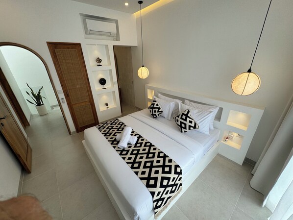 A modern hotel room with a large bed, a bedside table, a wall-mounted air conditioner, and a potted plant. - Playa Canggu 4 (Canggu)