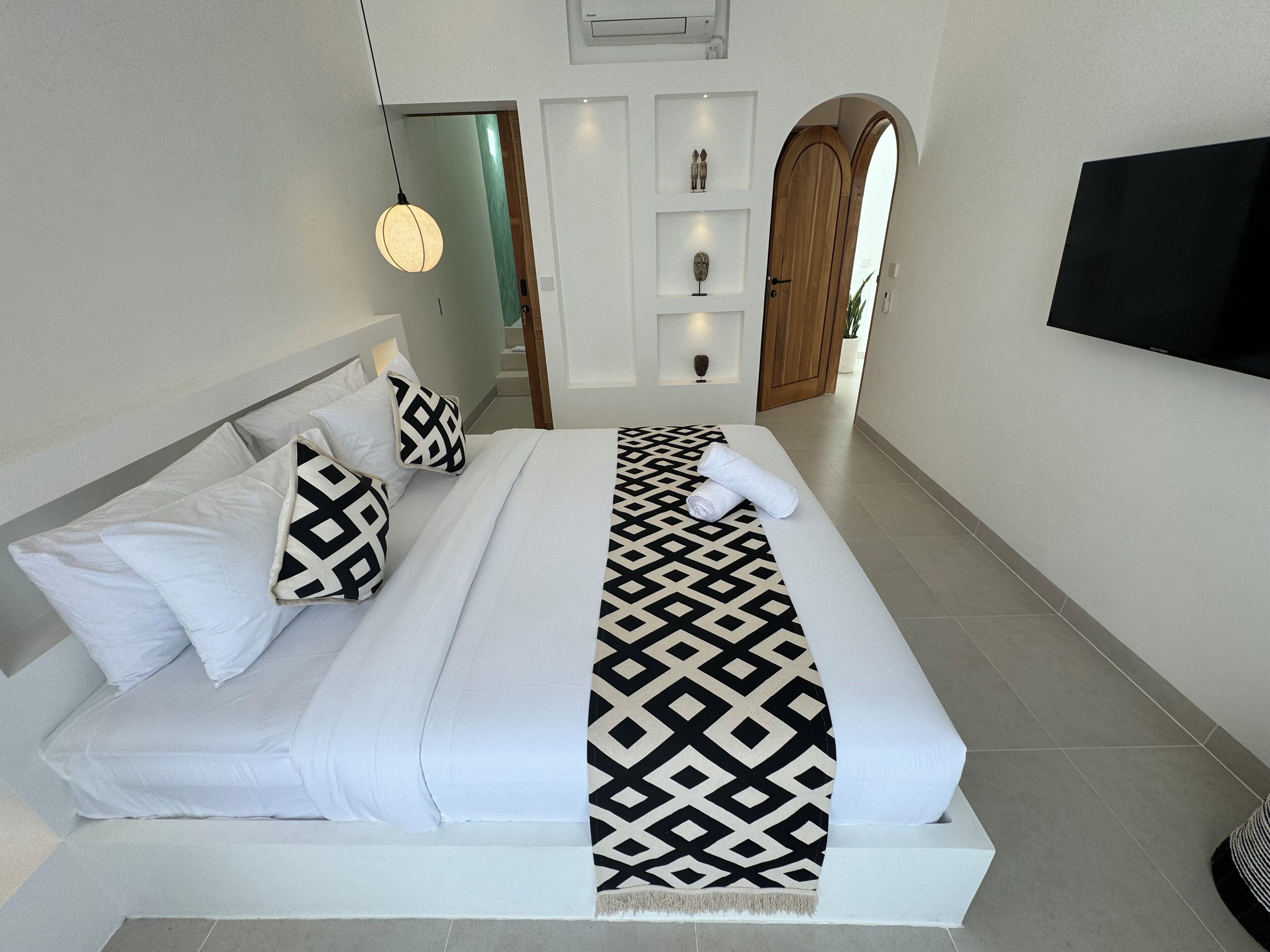 Una cama bien hecha con una colcha estampada, almohadas blancas y una toalla enrollada.