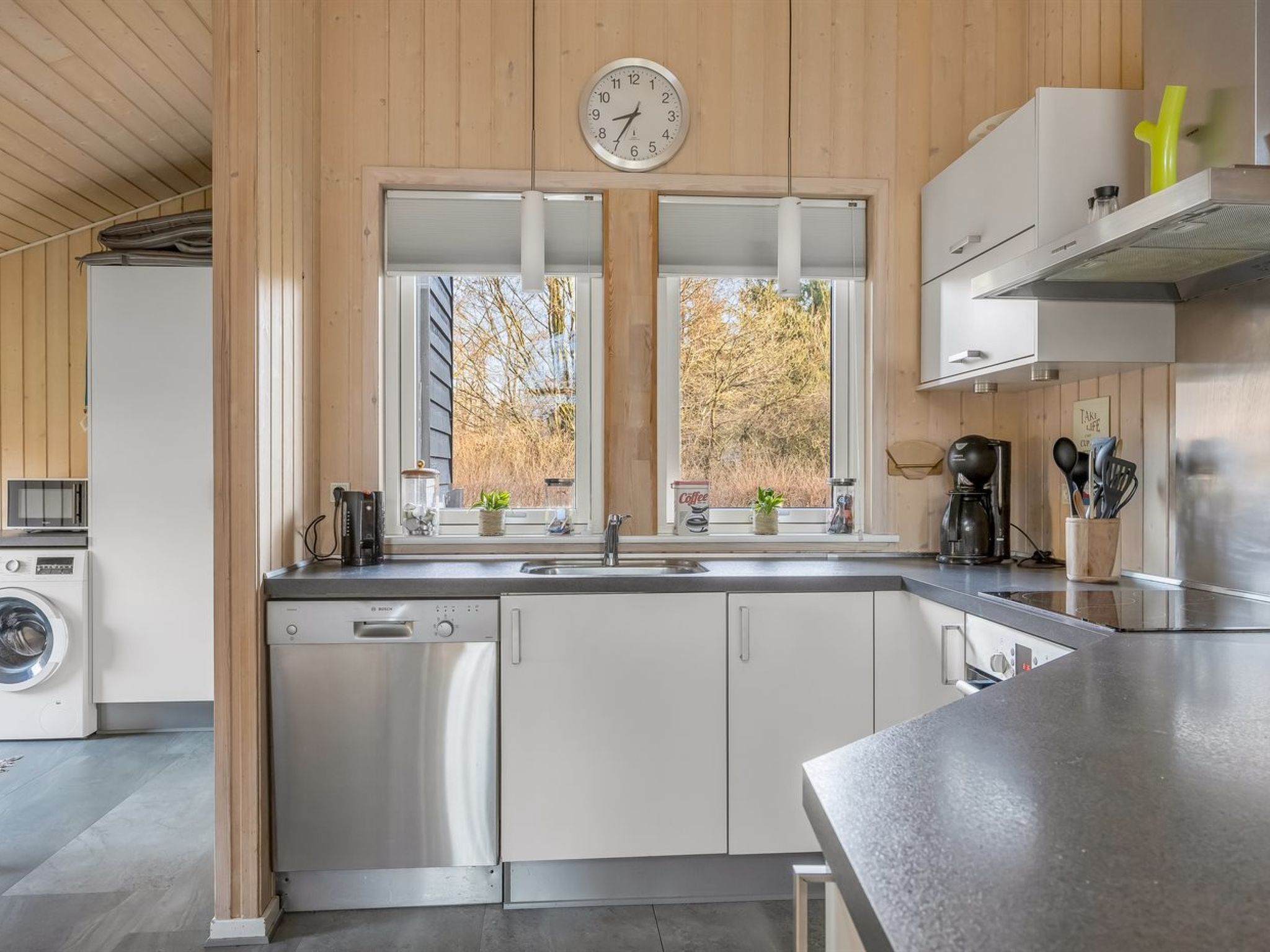A modern kitchen with stainless steel appliances, wooden paneling, a double sink, and a clock on the wall.