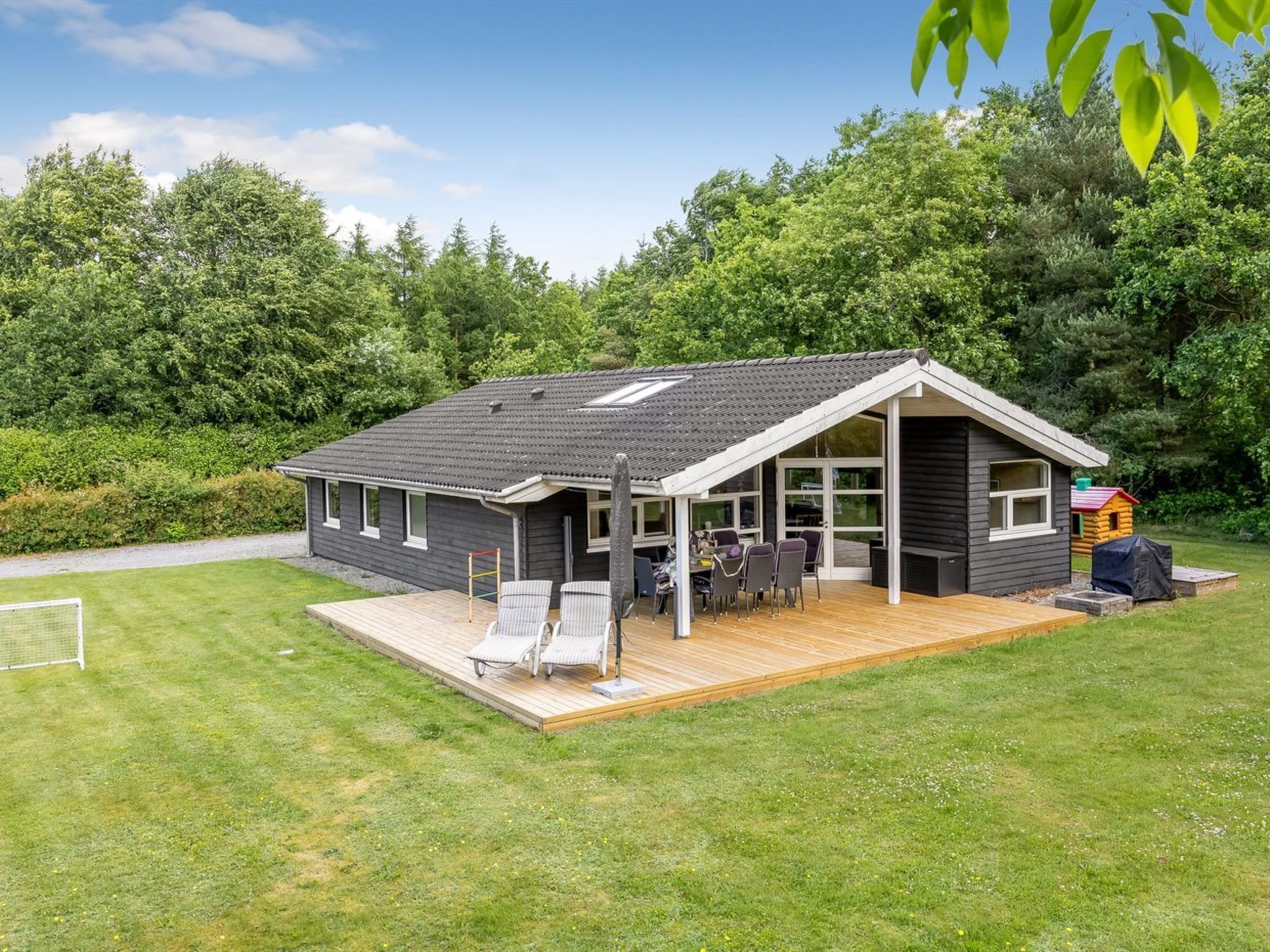 A single-story house with a deck, a patio with chairs, and a small playhouse in the background.