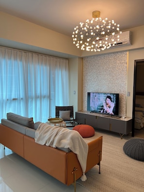 Ein modernes Wohnzimmer mit einer Couch, einem Fernseher und dekorativer Beleuchtung.