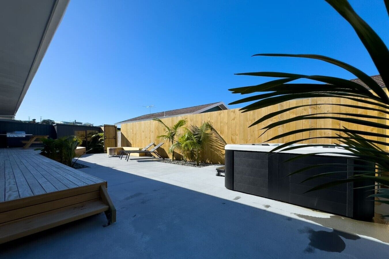 Une terrasse extérieure moderne, dotée d’une plateforme en bois, de chaises longues et d’un jacuzzi.