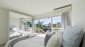 A hotel room with a large bed, a balcony with a view of the pool and palm trees, and an air conditioning unit on the wall. - Tranquil Retreat in Red Beach (Red Beach)