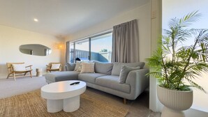 A modern living room with a grey sofa, a round coffee table, and a large window with curtains. - Tranquil Retreat in Red Beach (Red Beach)