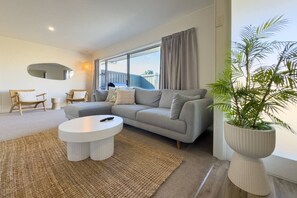 A modern living room with a grey sofa, a round coffee table, and a large window with curtains. - Tranquil Retreat in Red Beach (Red Beach)