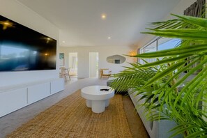A modern living room with a large flat-screen TV, a round coffee table, and a large plant.