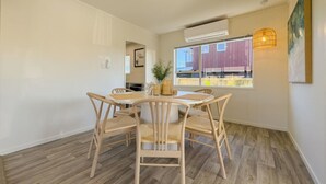 A dining area with a round table and four chairs, an air conditioning unit, a hanging light fixture, and a view of buildings outside. - Tranquil Retreat in Red Beach (Red Beach)