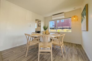 A dining area with a round table and four chairs, an air conditioning unit, a hanging light fixture, and a view of buildings outside. - Tranquil Retreat in Red Beach (Red Beach)
