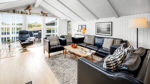 A spacious loft with a high ceiling, a black leather sofa set, a wooden coffee table, and a large window offering a view of the outdoors.