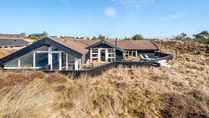 A modern beach house with a large deck, multiple rooms, and a view of the beach.