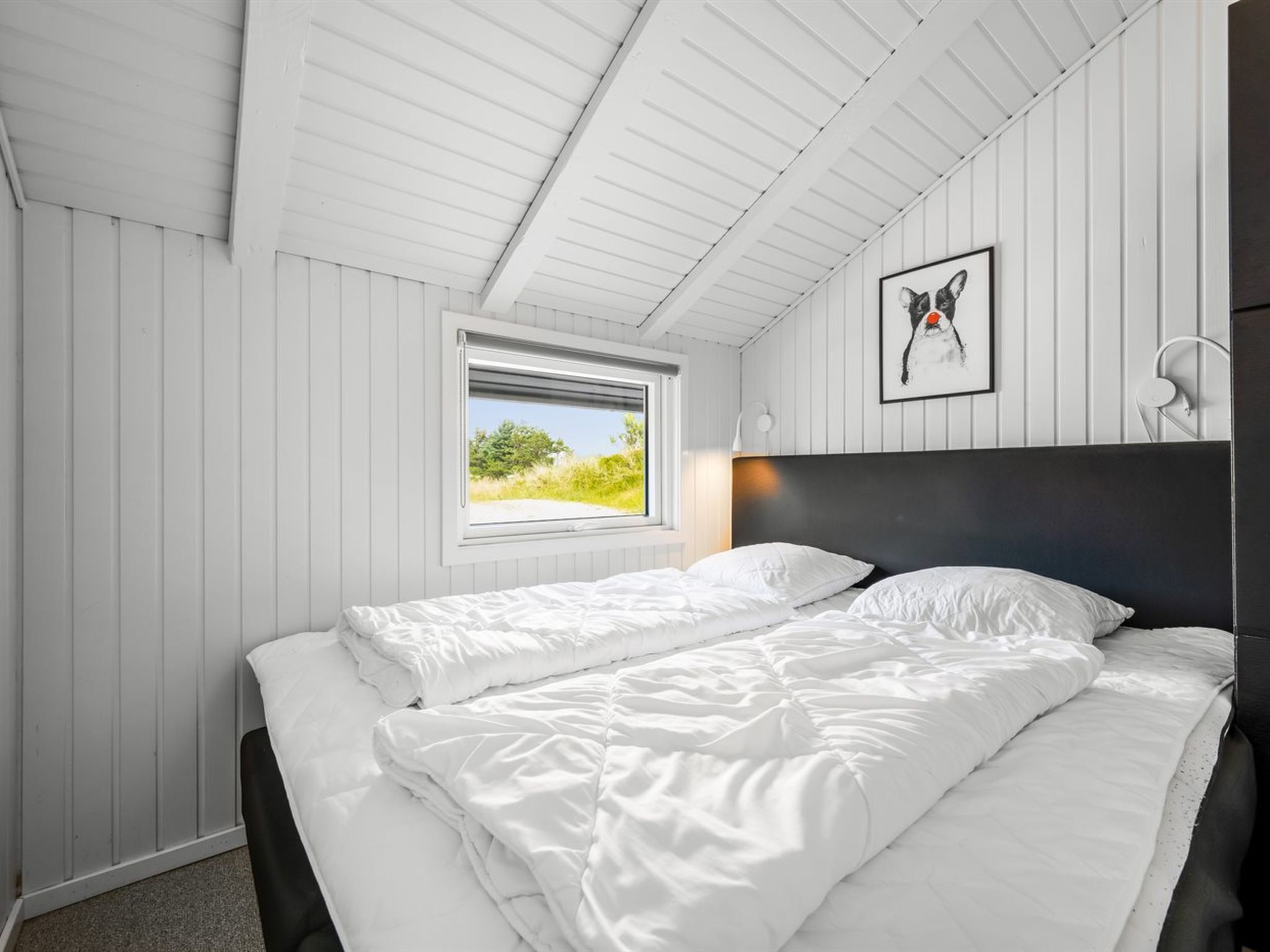 A bedroom with a bed, a window, and a framed picture on the wall.
